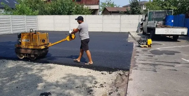 Kézi vezetésű kishenger tömöríti az új aszfaltot egy udvaron